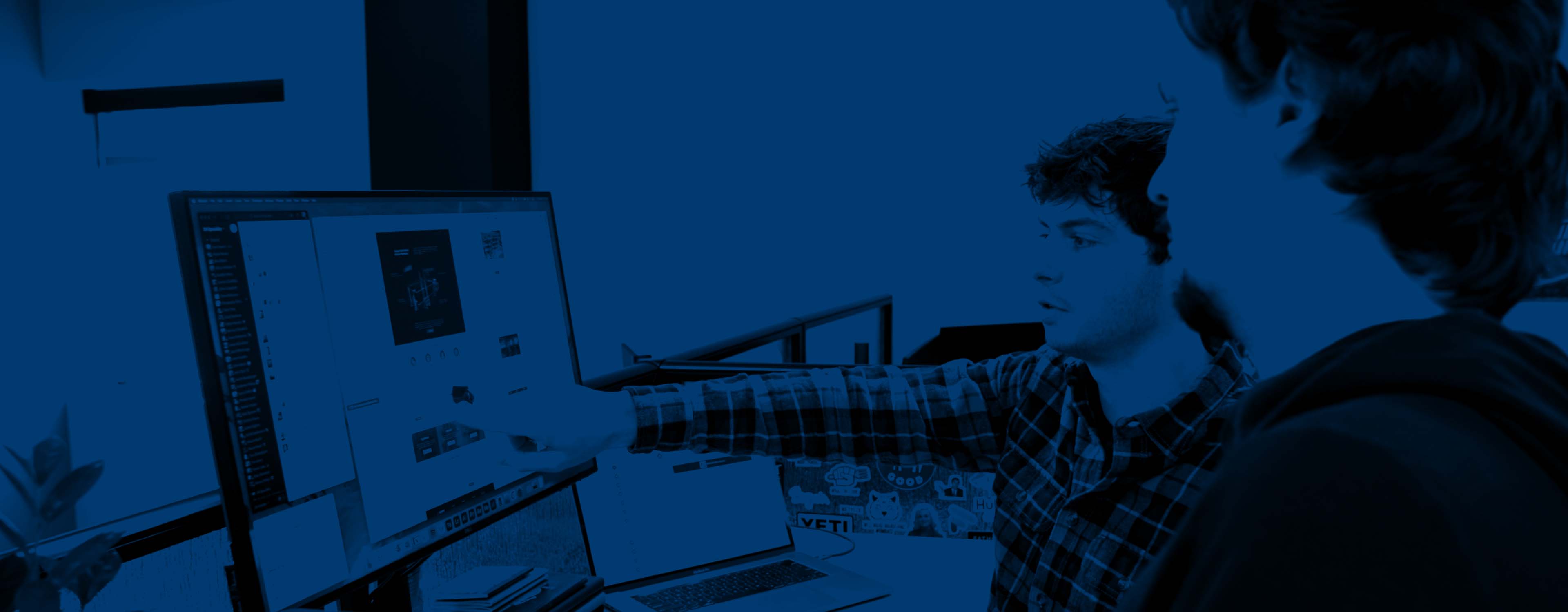 A duotone image of two people meeting and pointing at a computer screen.